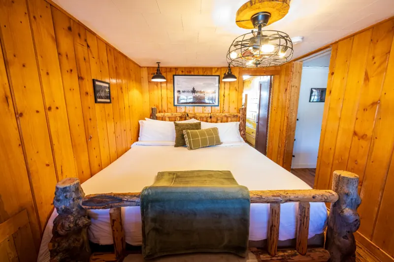 Cassidy Suite two bedroom cabin at The Amoretti Hotel in Dubois, Wyoming, a log frame bed with green throw pillows in a knotty pine bedroom.