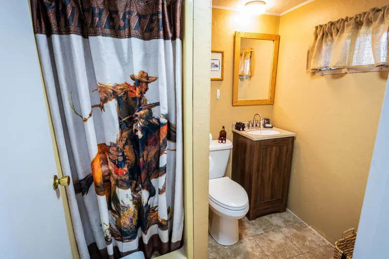 Cassidy Suite two bedroom cabin at The Amoretti Hotel in Dubois, Wyoming, the bathroom with a wood vanity, framed mirror, and a cowboy print shower curtain.
