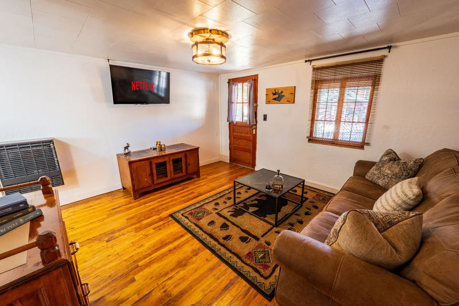 Cassidy Suite two bedroom cabin at The Amoretti Hotel in Dubois, Wyoming, the living room with a leather sofa, patterned rug, wood floors, and a wall mounted television.