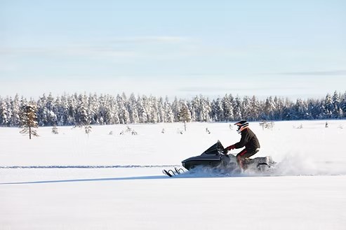 A rider carving across fresh powder on a snowmobile beneath snow covered evergreens, with Togwotee Pass near Dubois, Wyoming in winter