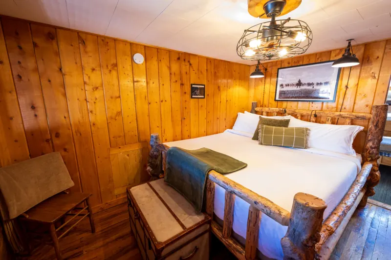 Cassidy Suite two bedroom cabin at The Amoretti Hotel in Dubois, Wyoming, a knotty pine bedroom with a log frame bed and a wrought iron light fixture.